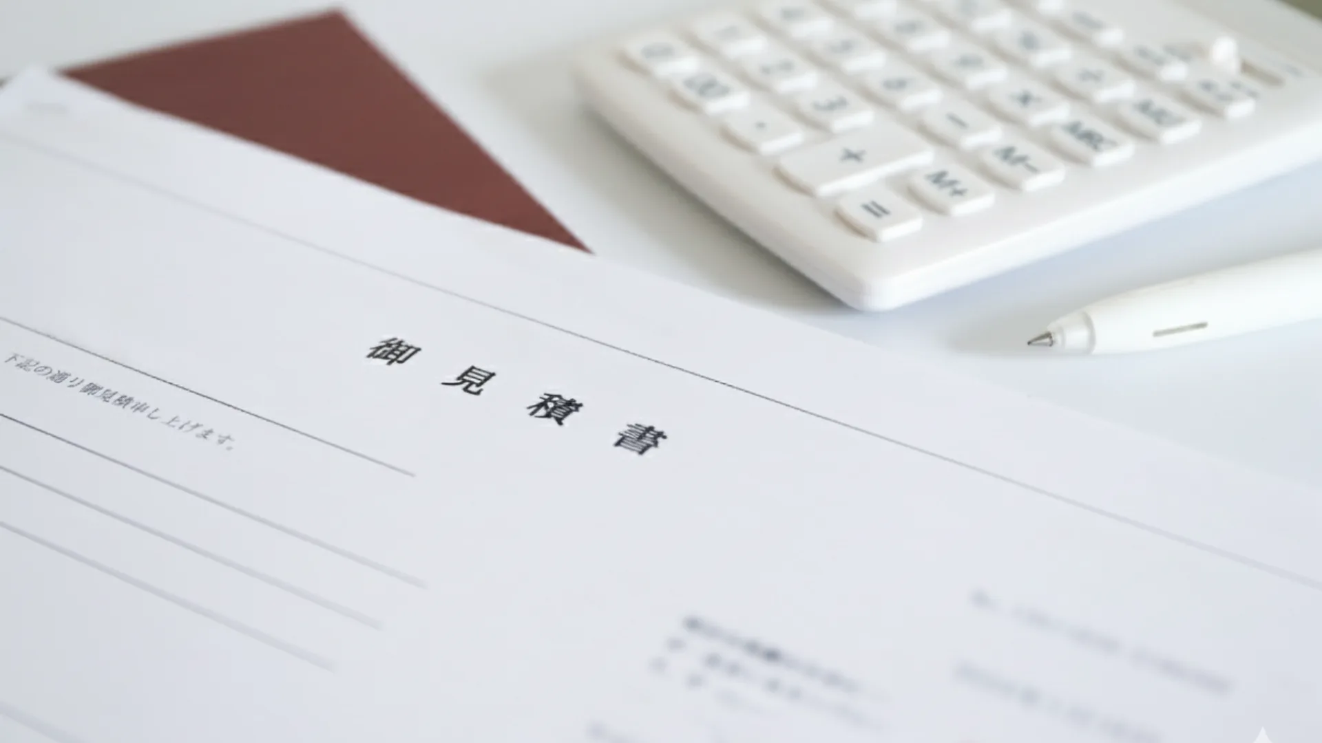 机の上に置かれた「工事見積書」と電卓、ペンの写真。建設業における正確な書類作成の重要性をイメージ。