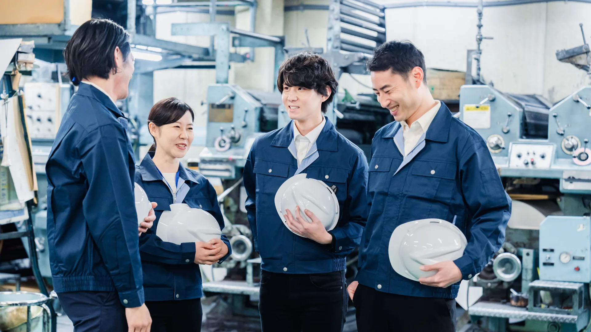 製造業の工場で笑顔でコミュニケーションをとる技術者・作業員4名、DX推進のためのチームビルディング