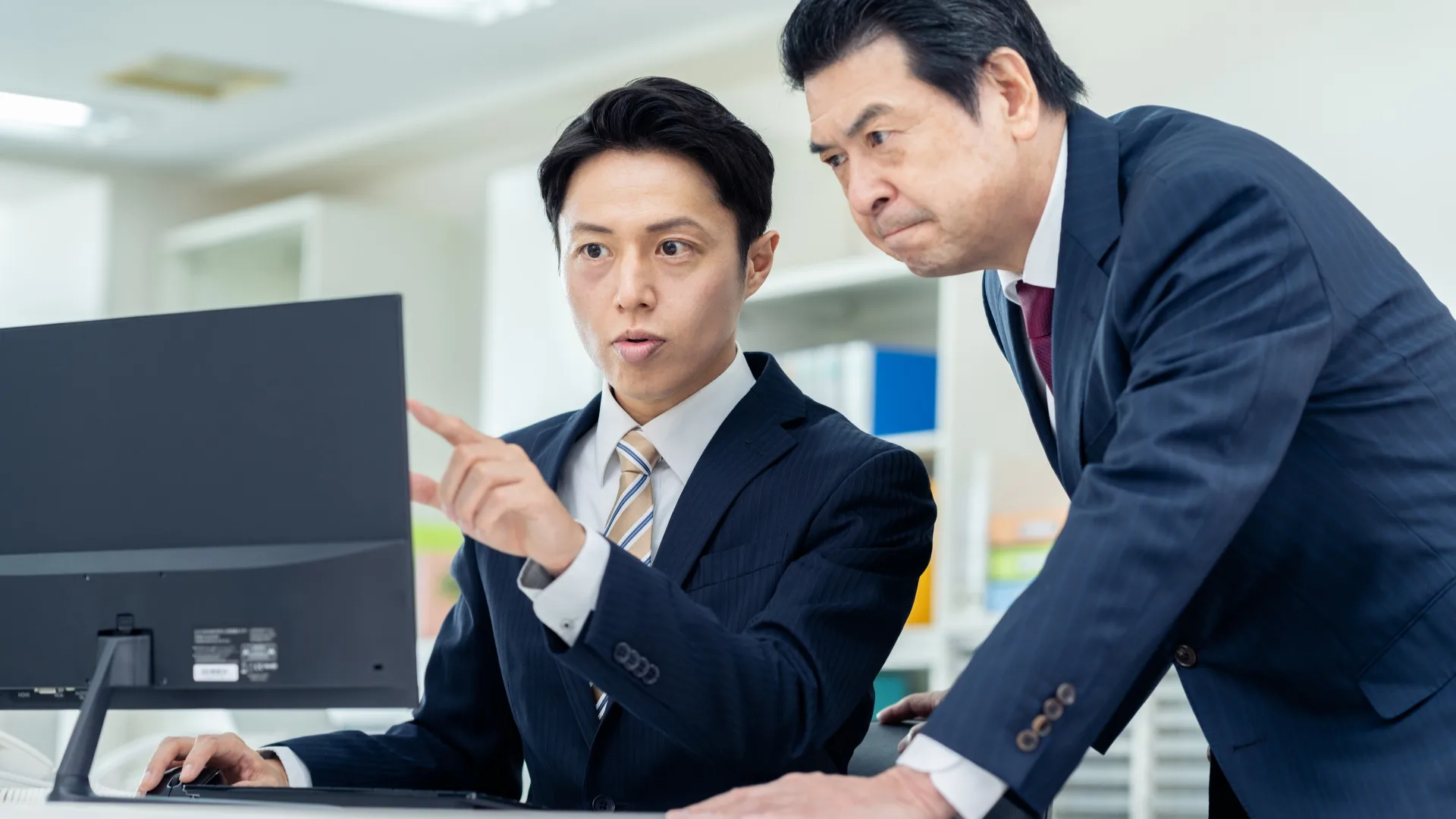 PC画面を指さし、RPA化におけるデメリットと課題を議論するビジネスマン