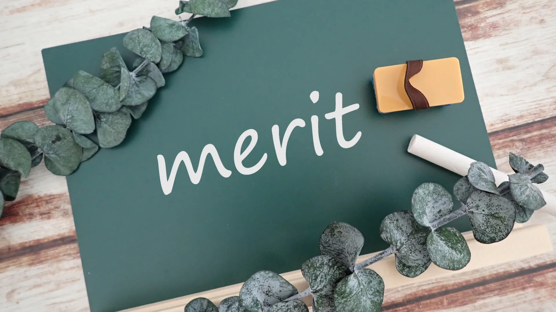 グリーンボードに「merit」と書かれた文字と、消しゴム・チョーク。
