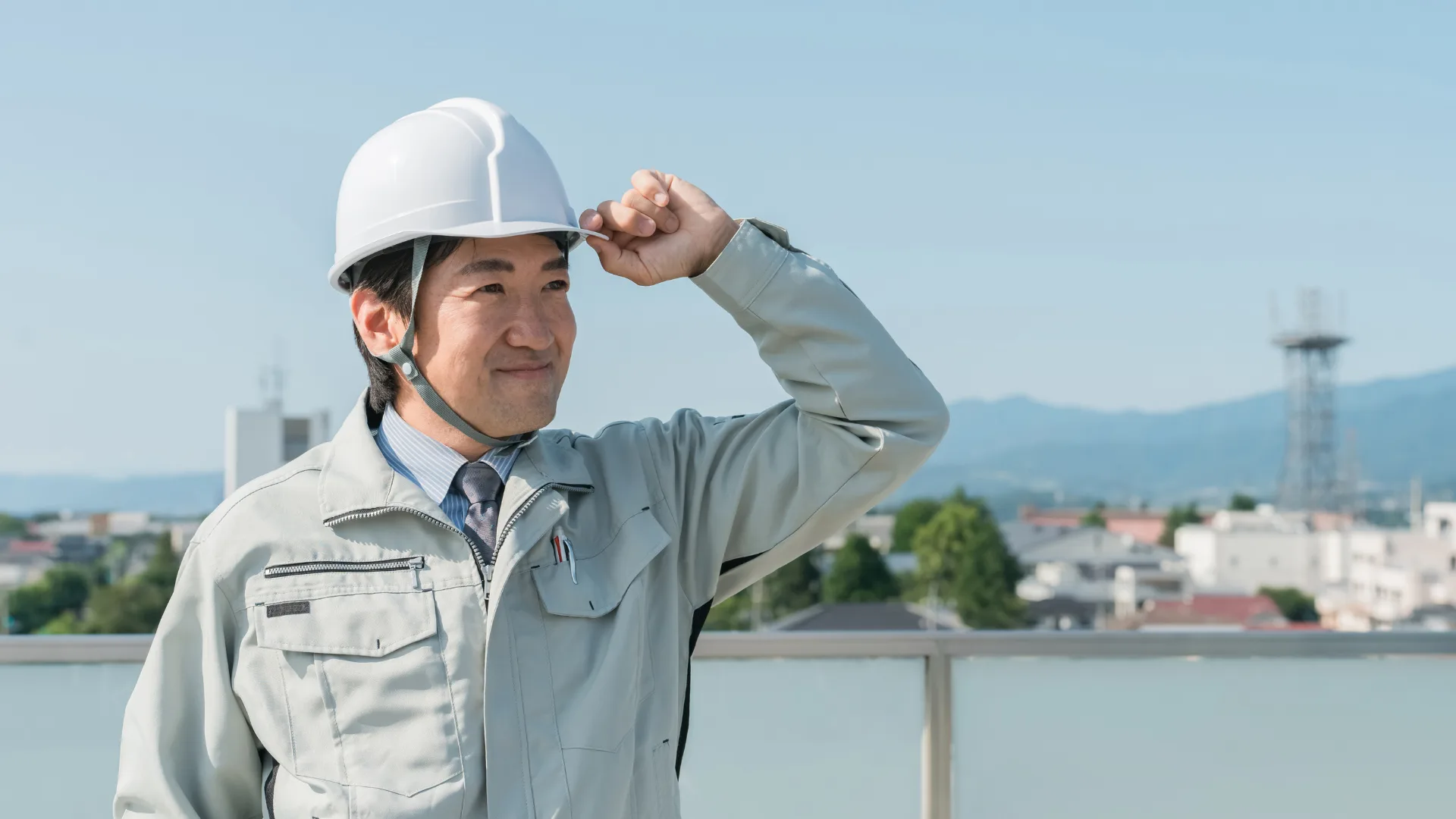 街並みを背にヘルメットに手を添えて見つめる作業員