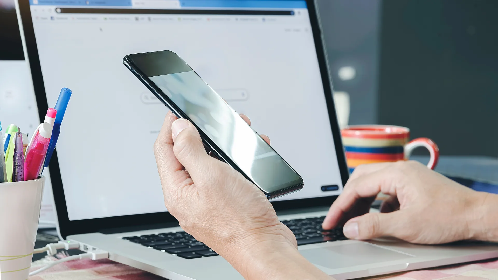 スマートフォンを持ちながらノートPCを操作する手元