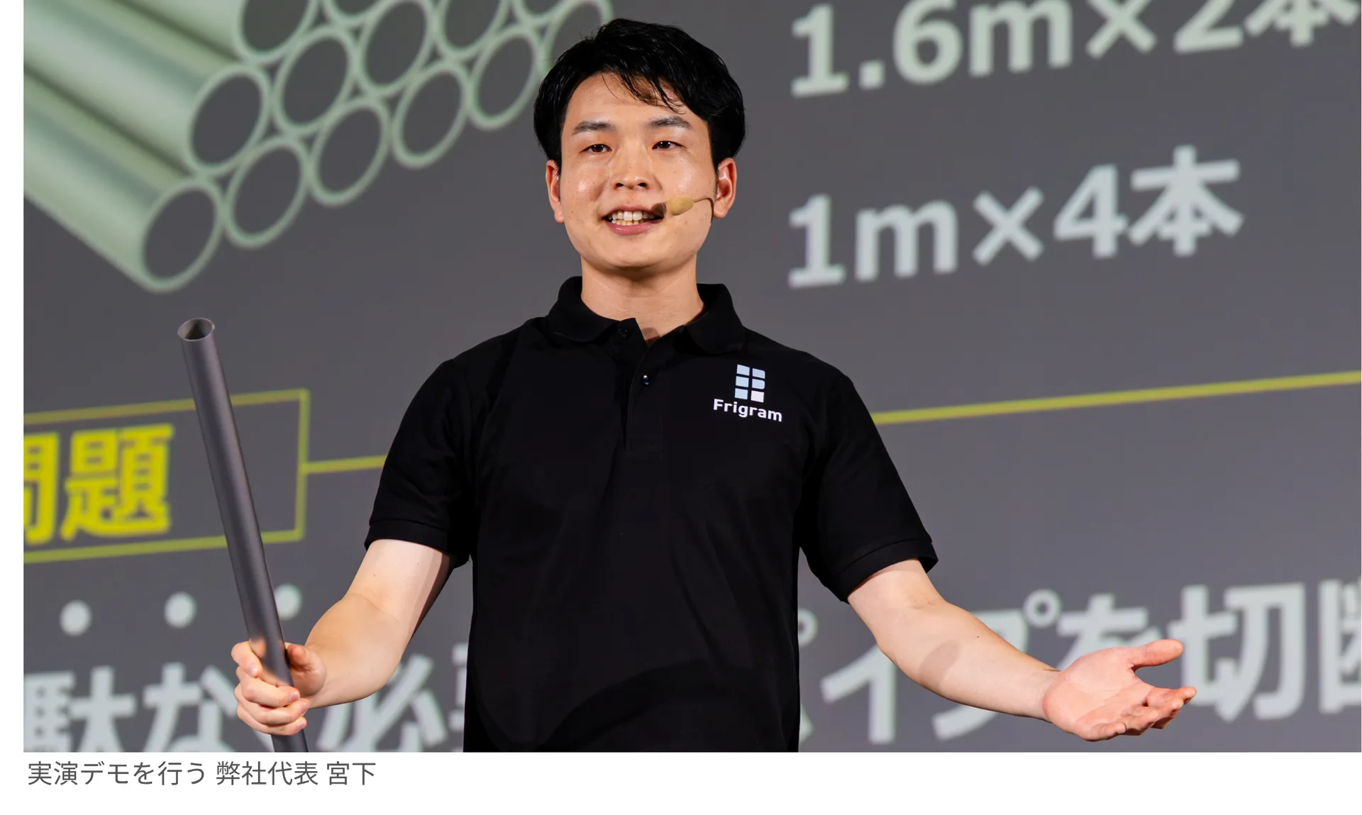実物のパイプを手に持ちながら切断最適化のデモを実演するフリグラム代表 宮下。背後のスクリーンに切断計画の数値が表示されている。