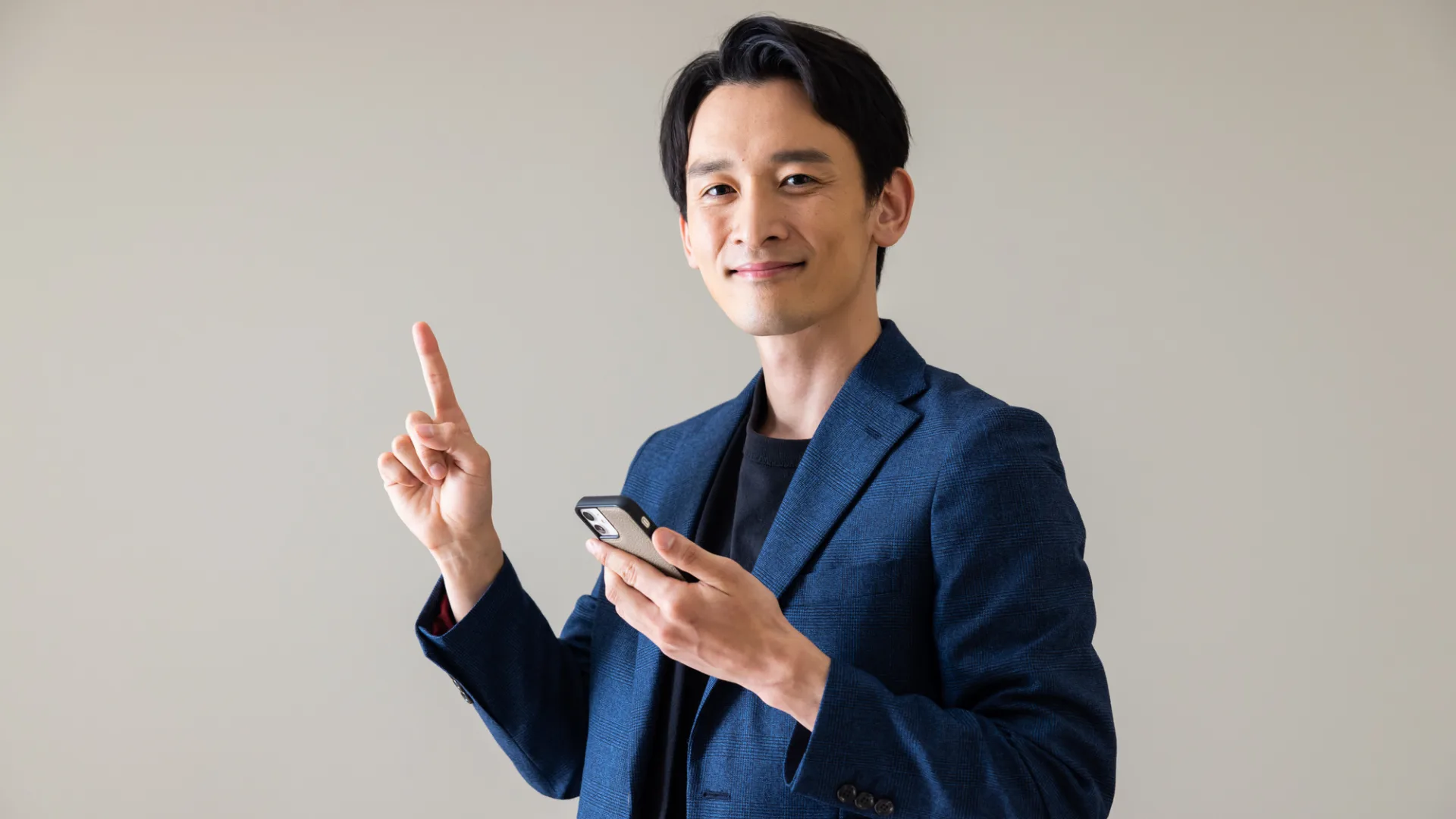 スマートフォンを持ち、指さしポーズをする笑顔のビジネスマンの男性。