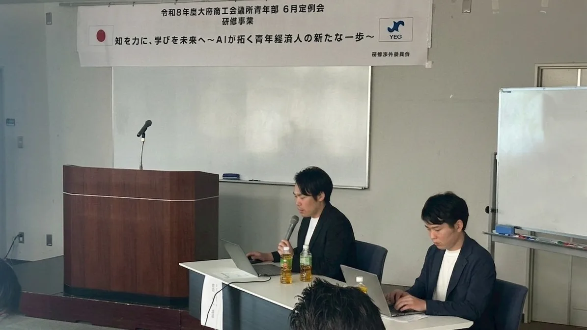 大府商工会議所青年部6月定例会のAIセミナーに登壇するフリグラム宮下代表（右）と株式会社BEAT X勝間代表（左）。会場正面には「知を力に、学びを未来へ〜AIが拓く青年経済人の新たな一歩〜」と書かれた横断幕が掲げられている