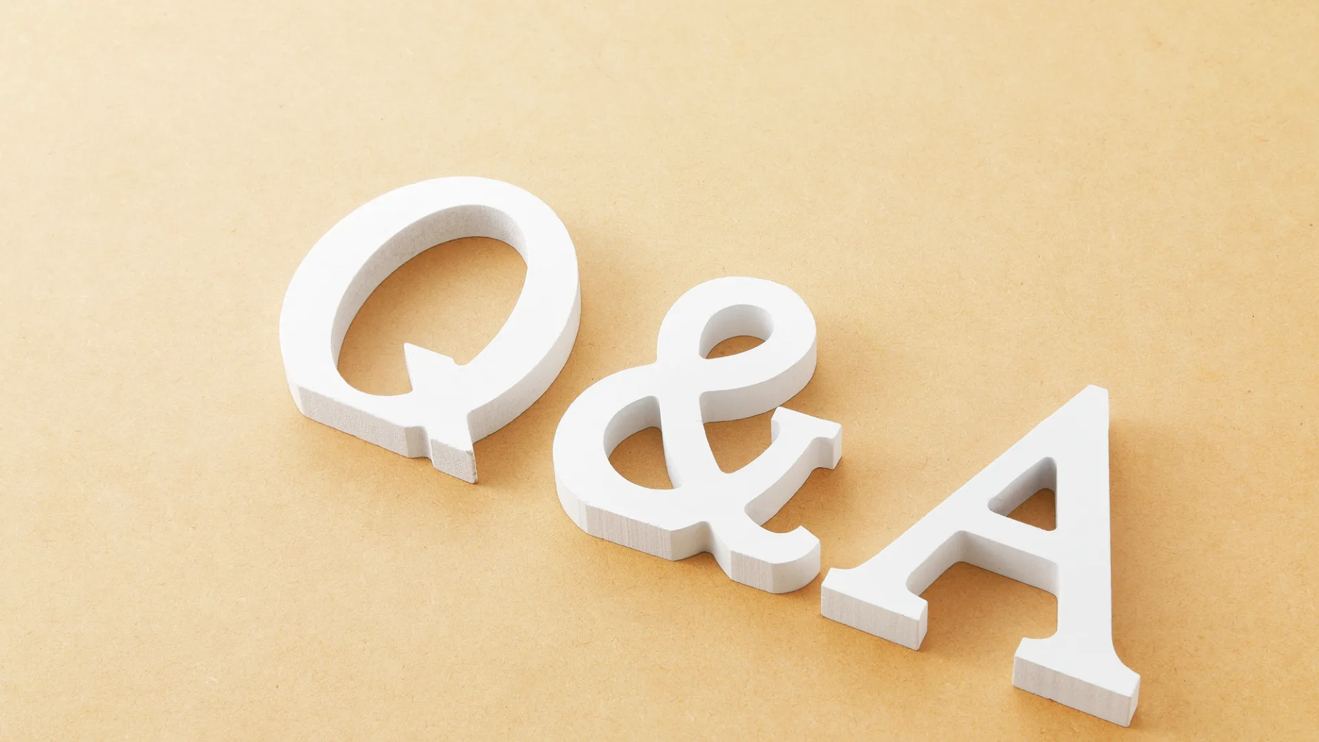 ベージュの背景に置かれた白い木製ブロックの「Q&A」の文字
