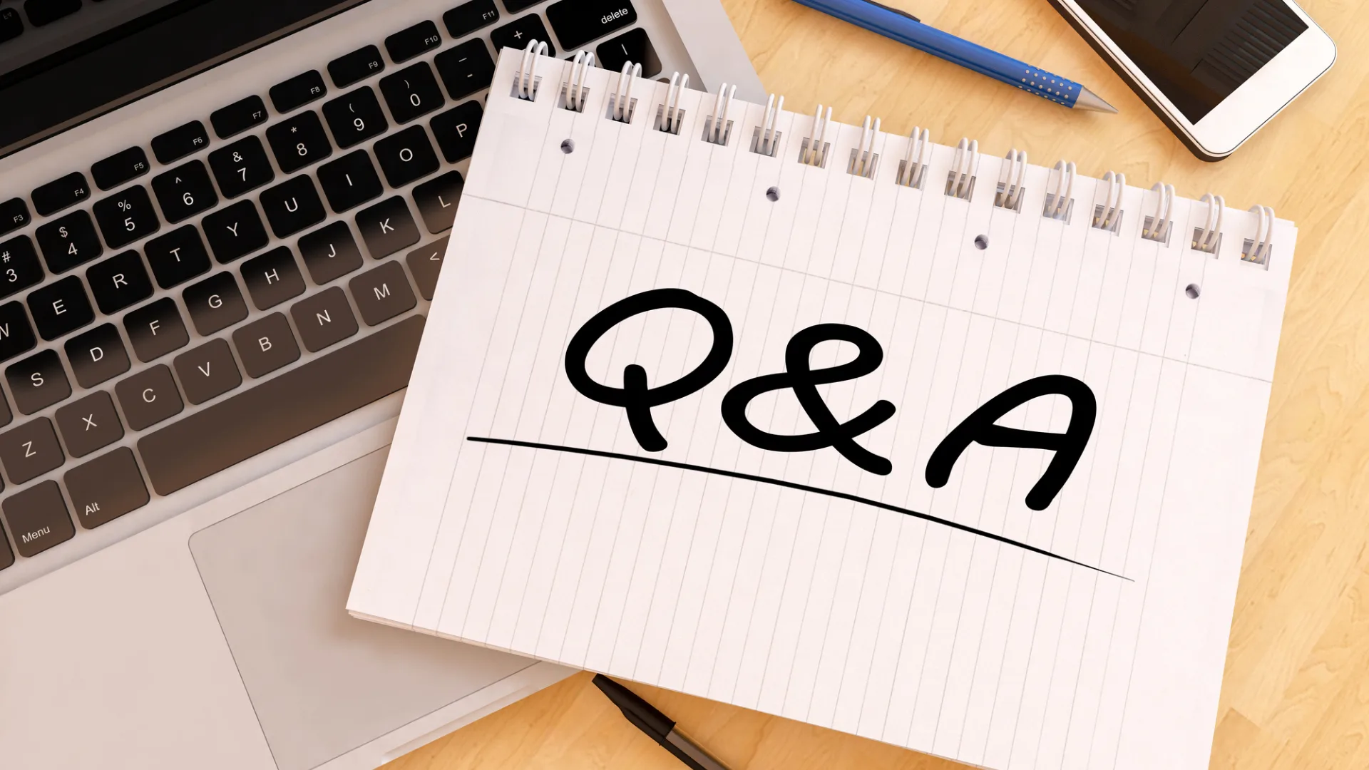 ノートPCの横に置かれたノートに「Q&A」と手書きされた文字。