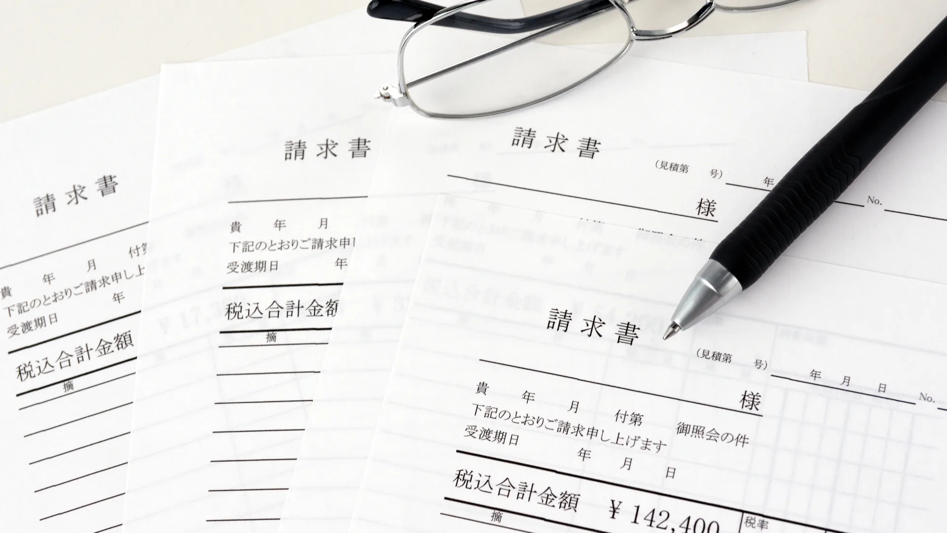 複数の請求書が重なり、その上に眼鏡とペンがクローズアップ