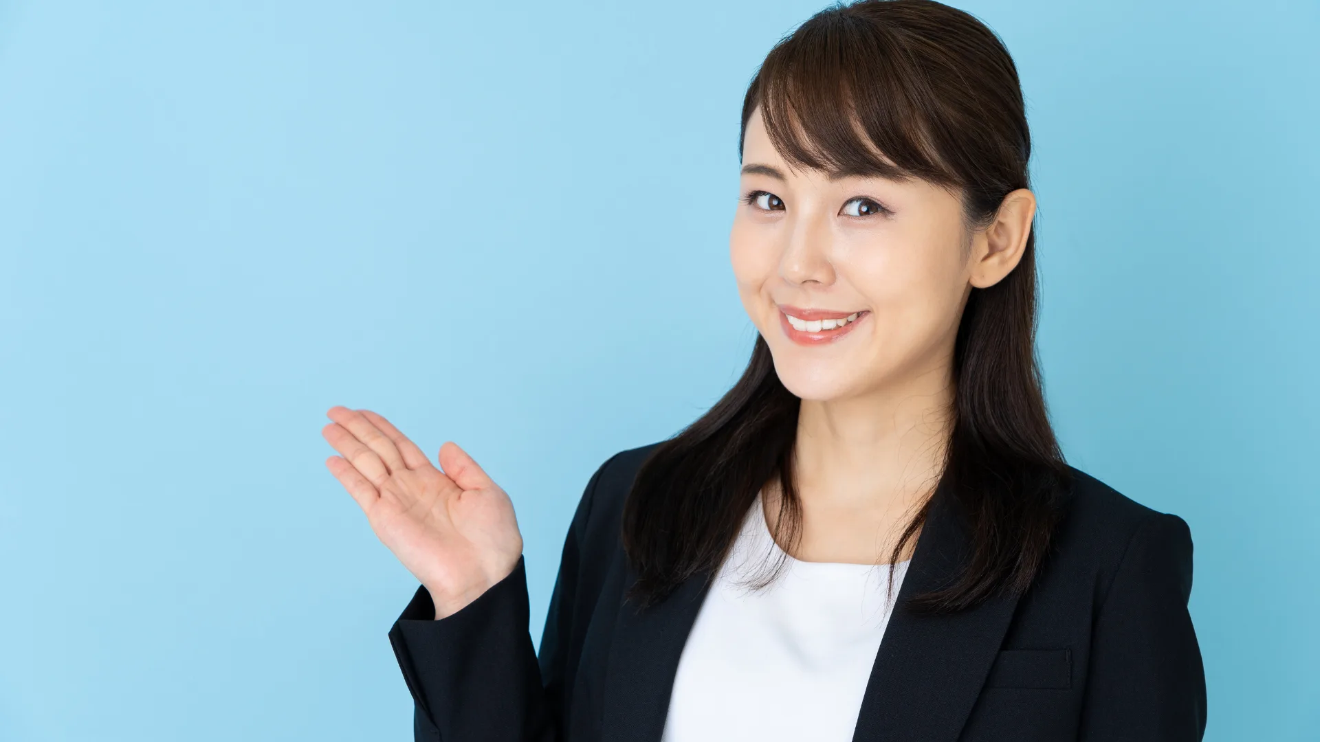 右手をこちらと差し出すジャケット姿のビジネスウーマン。