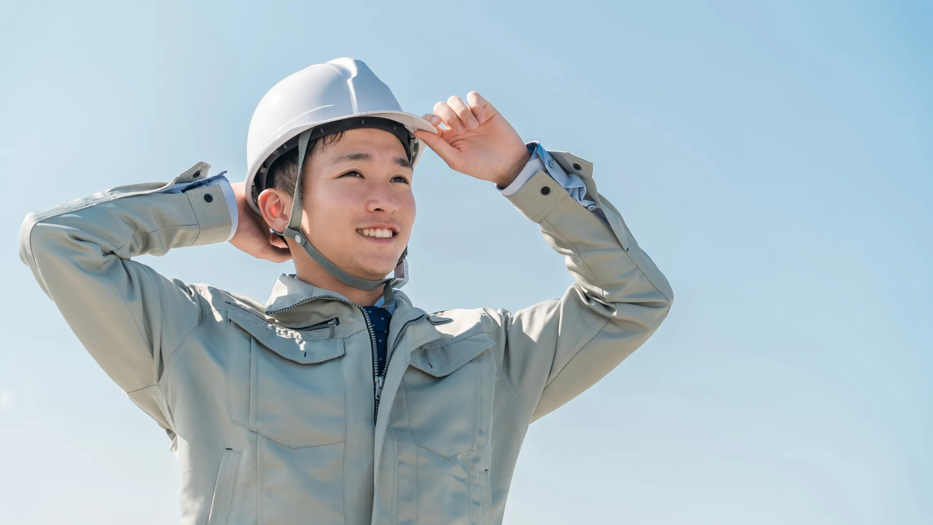 青空の下、ヘルメットを被った笑顔の建設作業員。適切な見積書作成を通じて信頼関係を築き、ビジネスが成功するイメージ。